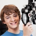 Smiling boy holding phoropter while undergoing an eye examinatio